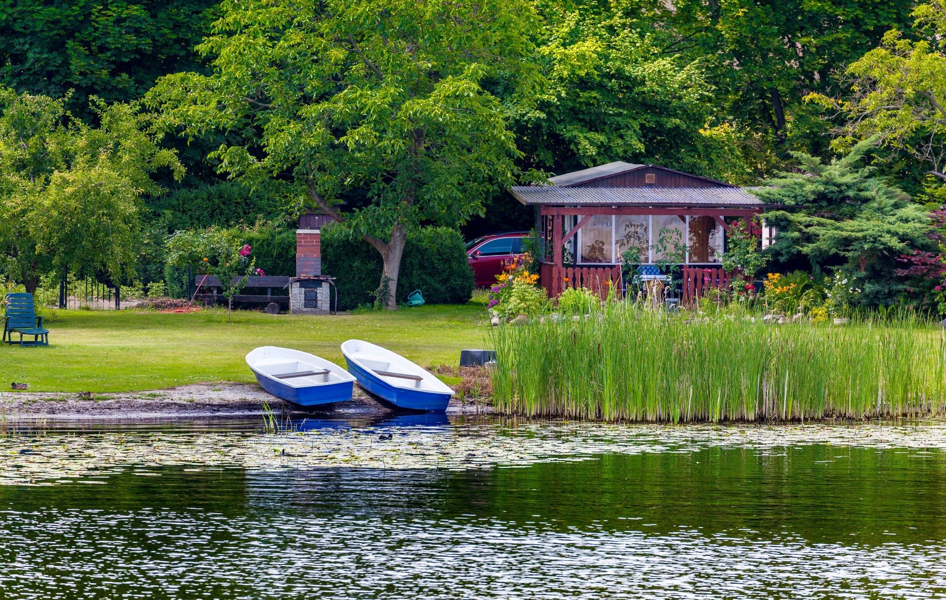 Kleines Holzhaus mit Booten an einem Seeufer, umgeben von Bäumen und Garten – typisch für Wochenendgrundstücke ohne Kanalanschluss